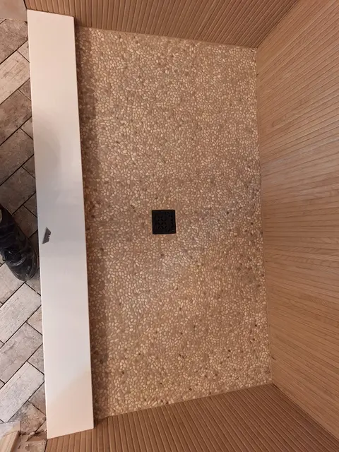 Shower wall covered in pebble stone mosaic with a black drain fixture, Kings Mountain Tile project in North Carolina