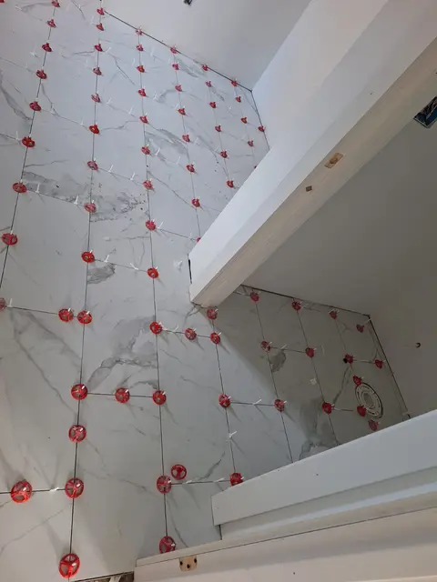 Marble-look floor tiles laid with leveling clips around a bathroom corner, Kings Mountain Tile project in North Carolina