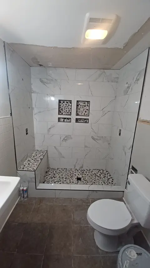 Marble-look tile shower with bench, pebble floor and decorative niches
