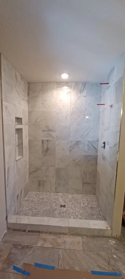 Large-format marble tile shower with built-in niches and pebble floor